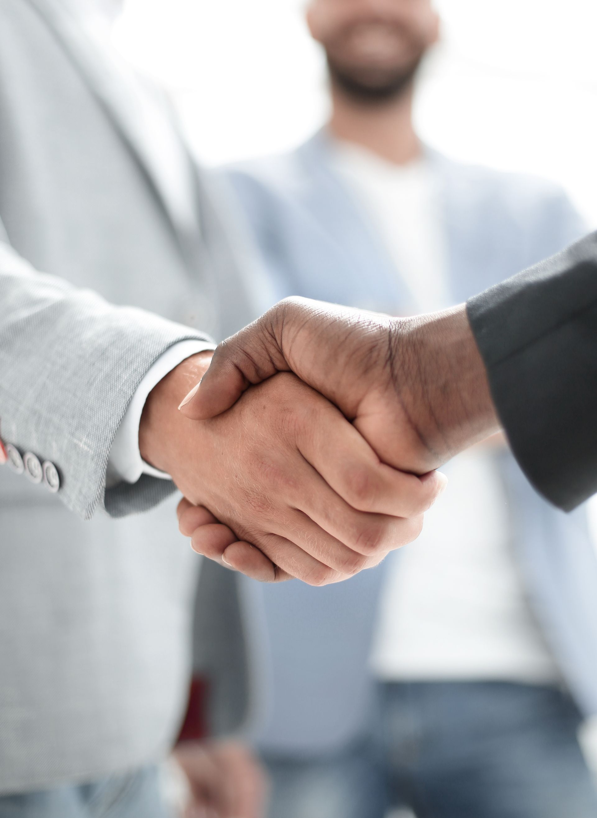 Two people shaking hands, blurred background of two others, business setting.