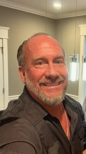 Man with a beard smiling, wearing a dark shirt, indoors.