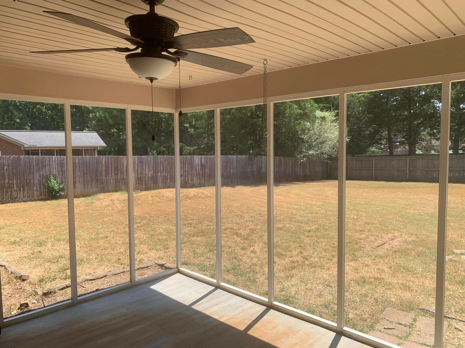 Screened patio overlooking a dry backyard with a ceiling fan and wooden fence