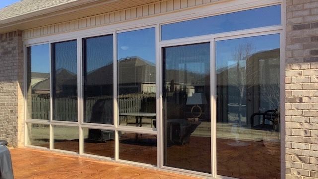 Large sliding glass doors and windows on a brick house patio, reflecting the outdoor deck.