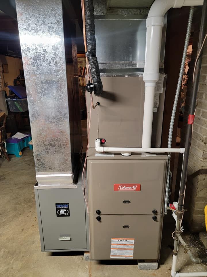 A furnace is sitting in a basement next to a heater.
