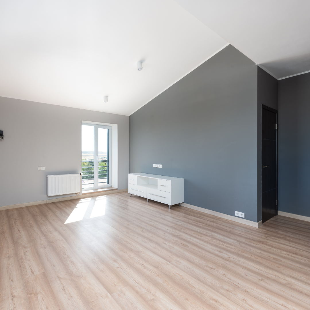 An empty living room with a wooden floor and gray walls.