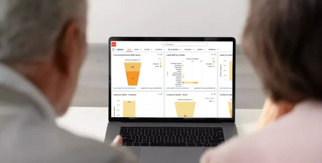 Uma mulher está falando em uma videochamada enquanto mostra a Dashboard Labora e olha para um painel em um tablet.