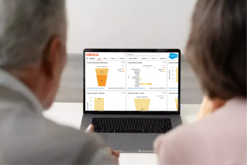 Uma mulher está falando em uma videochamada enquanto mostra a Dashboard Labora e olha para um painel em um tablet.