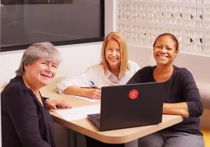 Três mulheres estão sentadas à mesa com um laptop.
