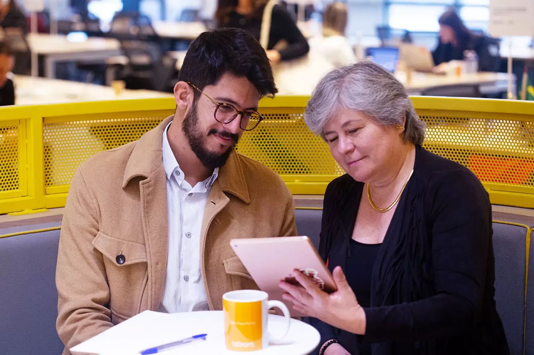 Um homem e uma mulher estão sentados à mesa olhando para um tablet.