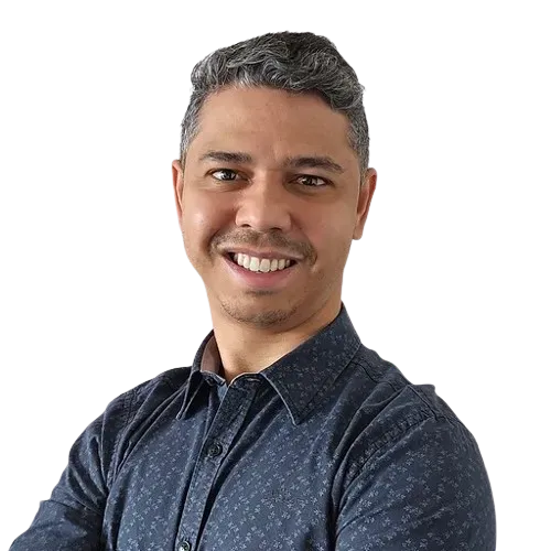 Um homem de camisa azul está sorrindo com os braços cruzados.