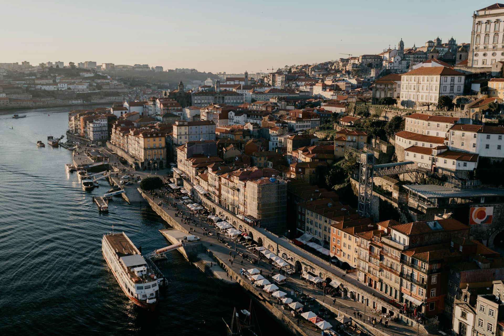 Paisagem urbana do Porto, Portugal, com edifícios ao longo do rio Douro, barcos e luz solar.