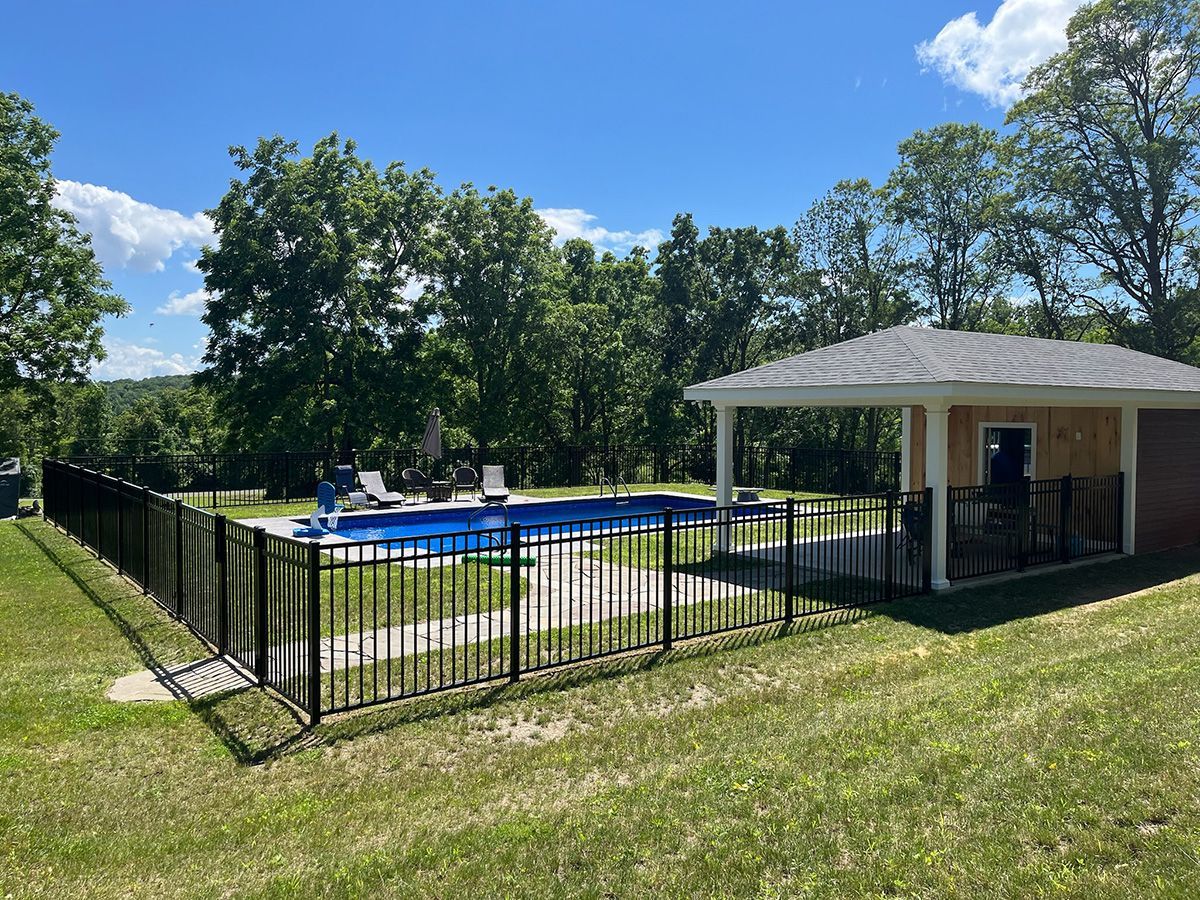 Black metal fence surrounds a concrete patio next to a two-story beige house and an attached sunroom.