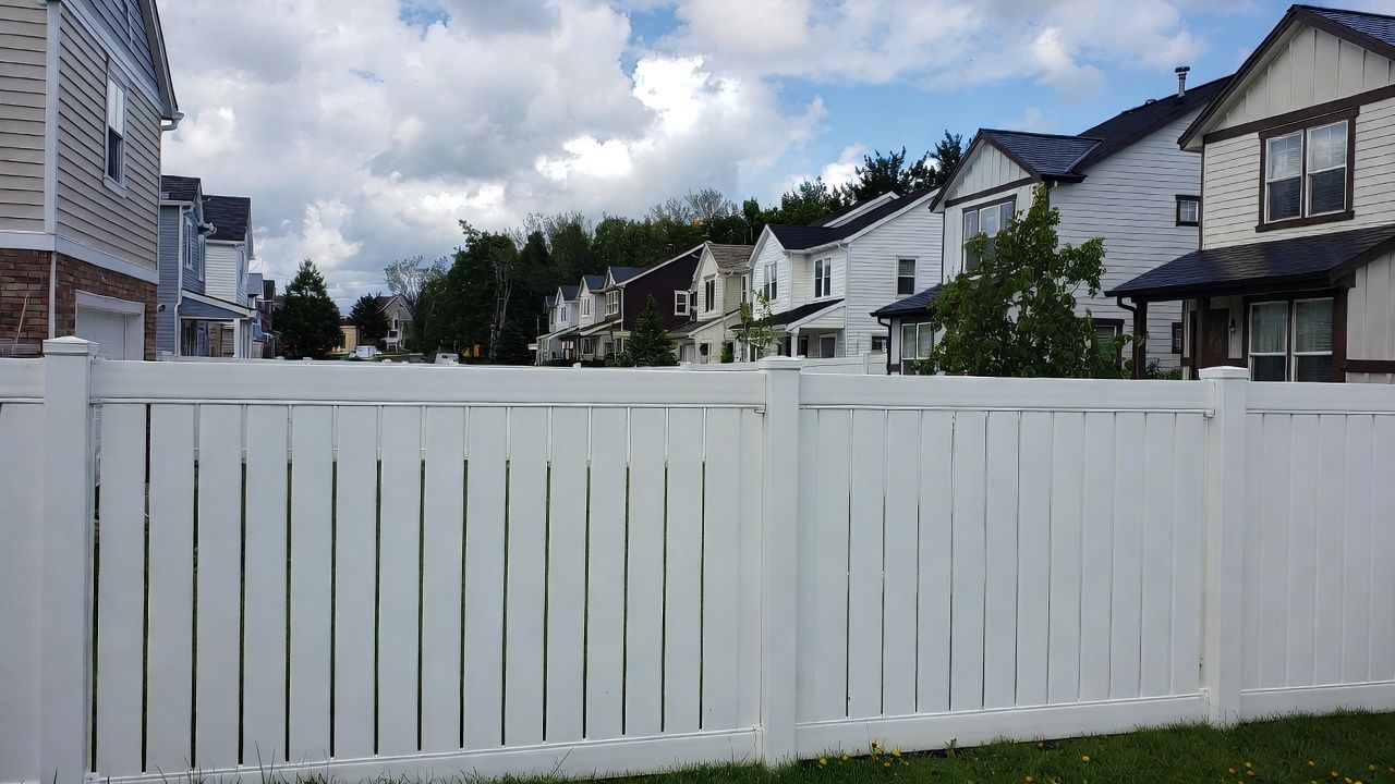 White picket fence in front of a neighborhood of houses under a cloudy sky.