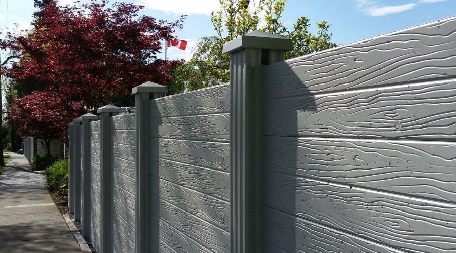 Soundproof grey concrete privacy fence with faux-wood texture.
