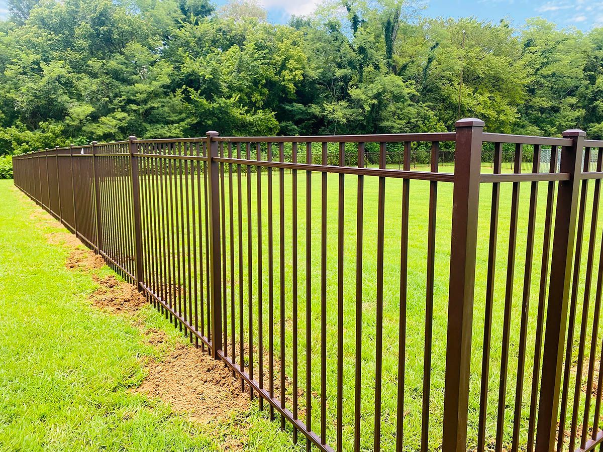 Black metal fence surrounds a concrete patio next to a two-story beige house and an attached sunroom.