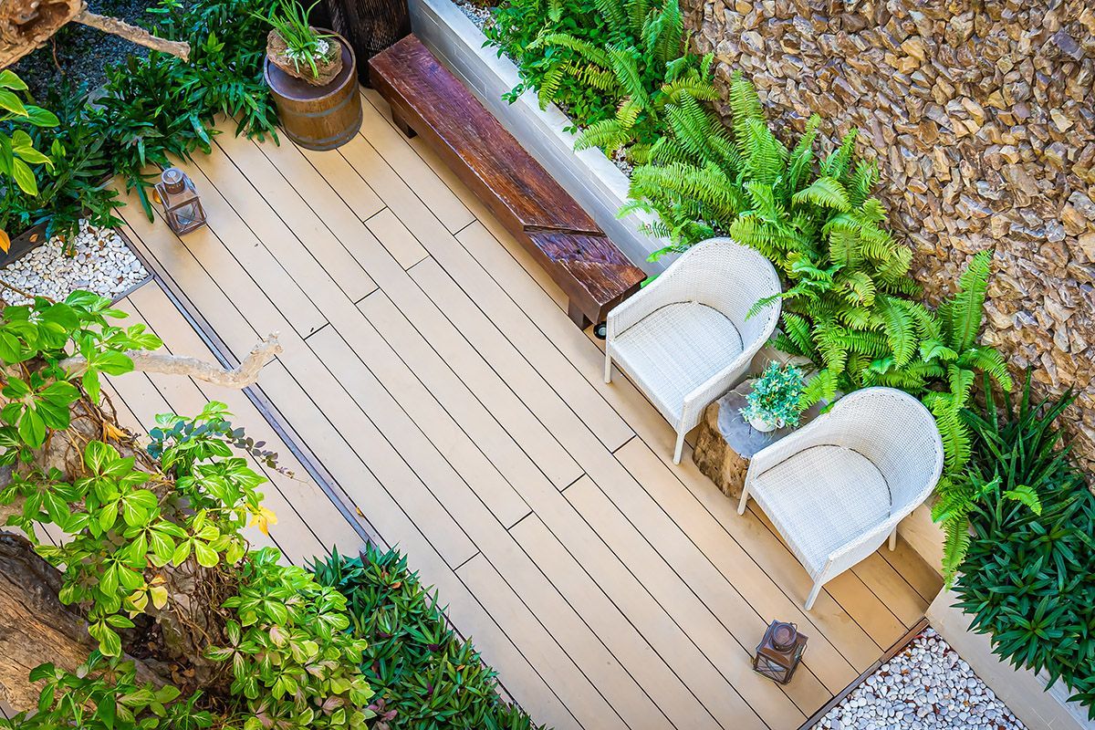 Overhead view of a small patio with two white chairs, wooden bench, and surrounding greenery.