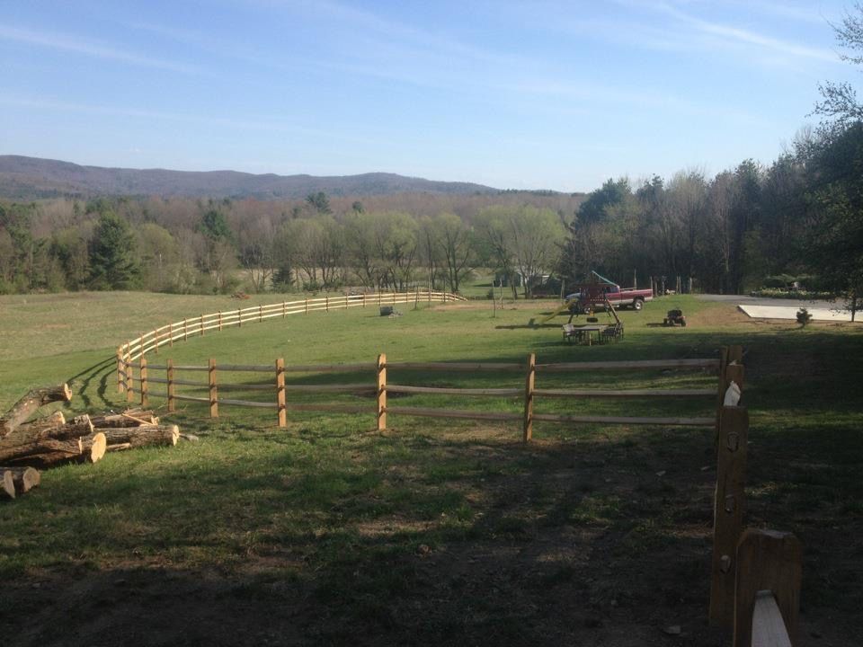 Green field with wooden fence; a distant mountain range and trees visible.