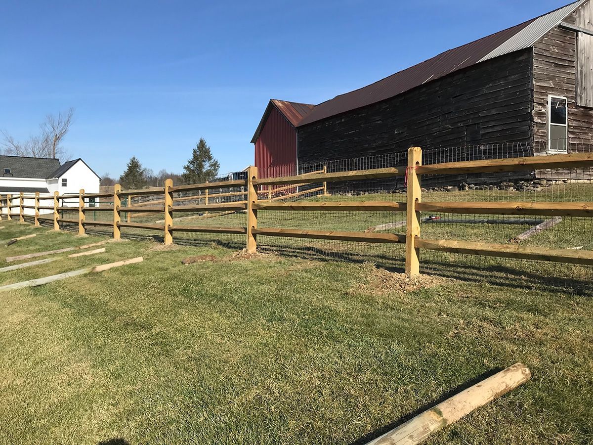 Wooden split-rail fence in a grassy field, with a barn in the background on a sunny day.
