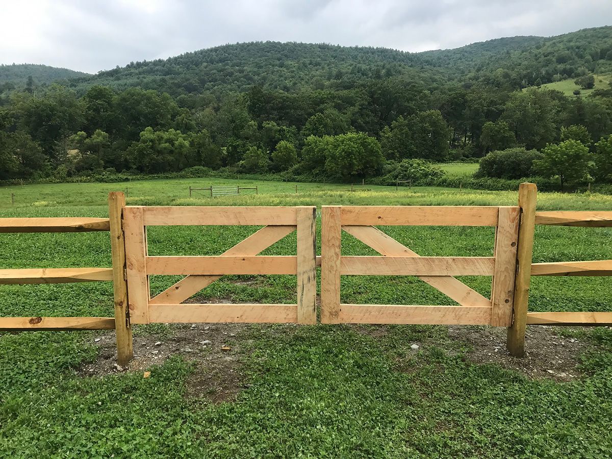 Wooden gate in a grassy field, with a forested mountain range in the background under a cloudy sky.