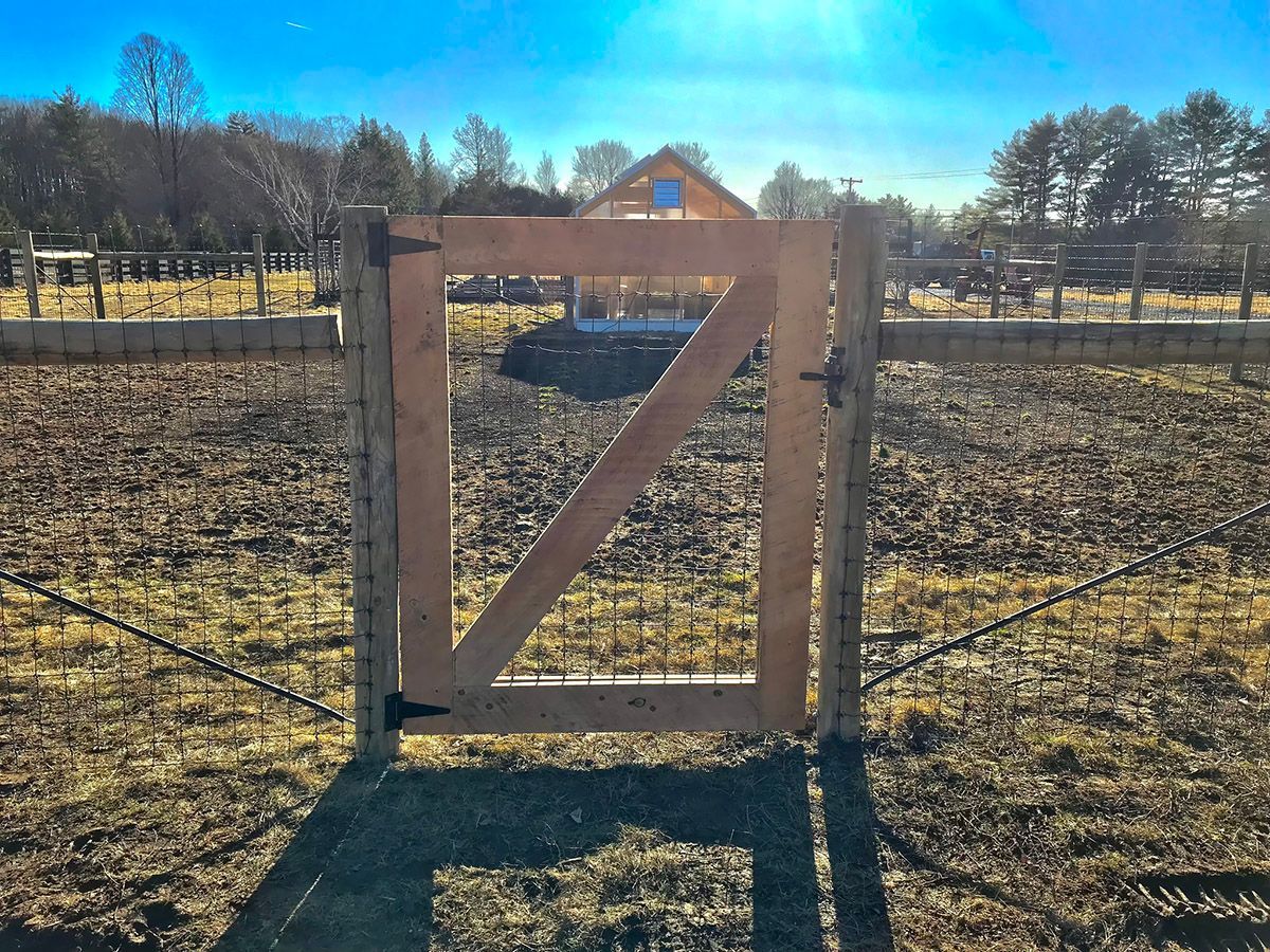 Wooden gate in a field, leading to a building under a bright blue sky.