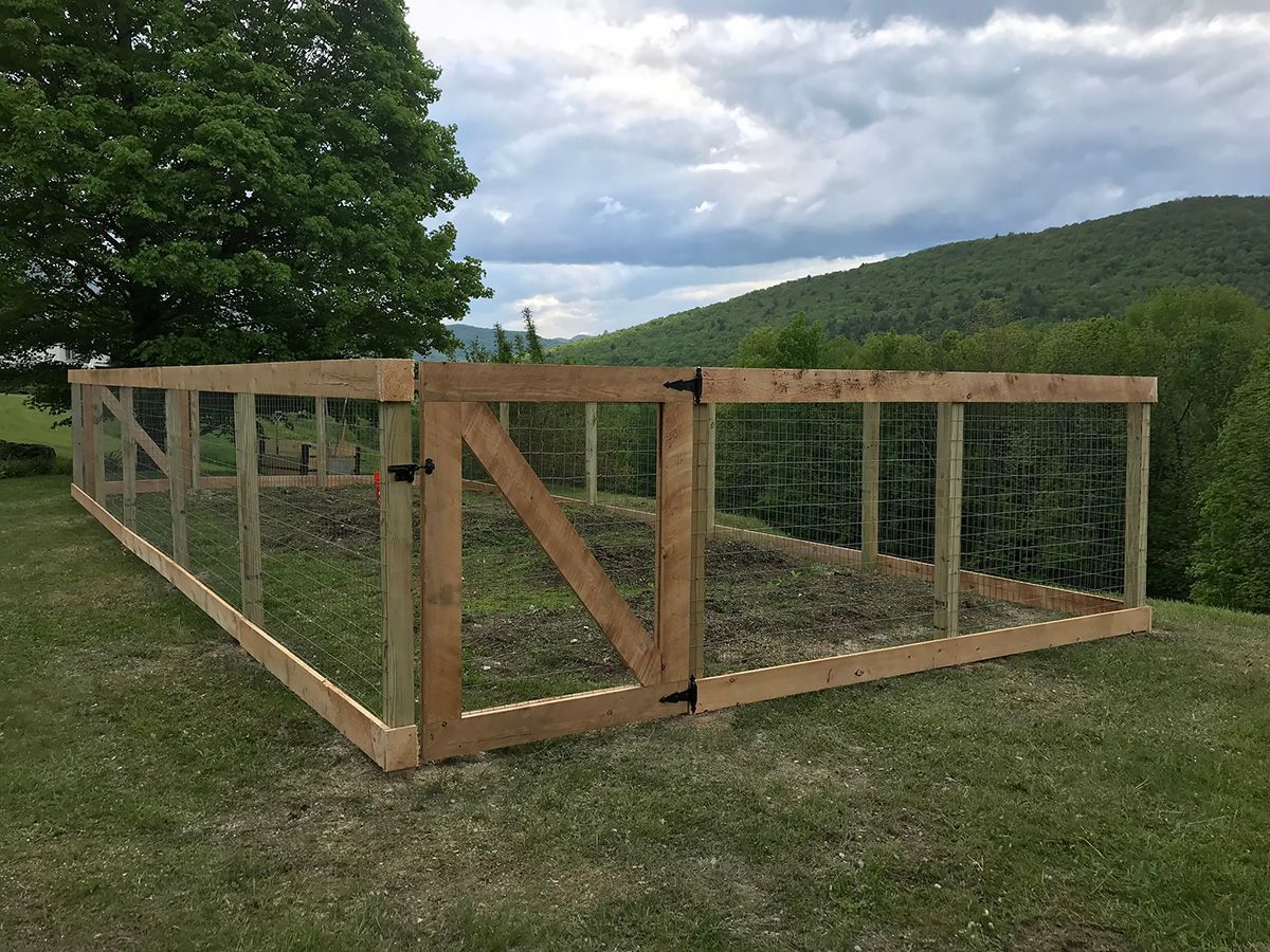 Wooden fence enclosure with wire mesh, gate, and hillside backdrop.