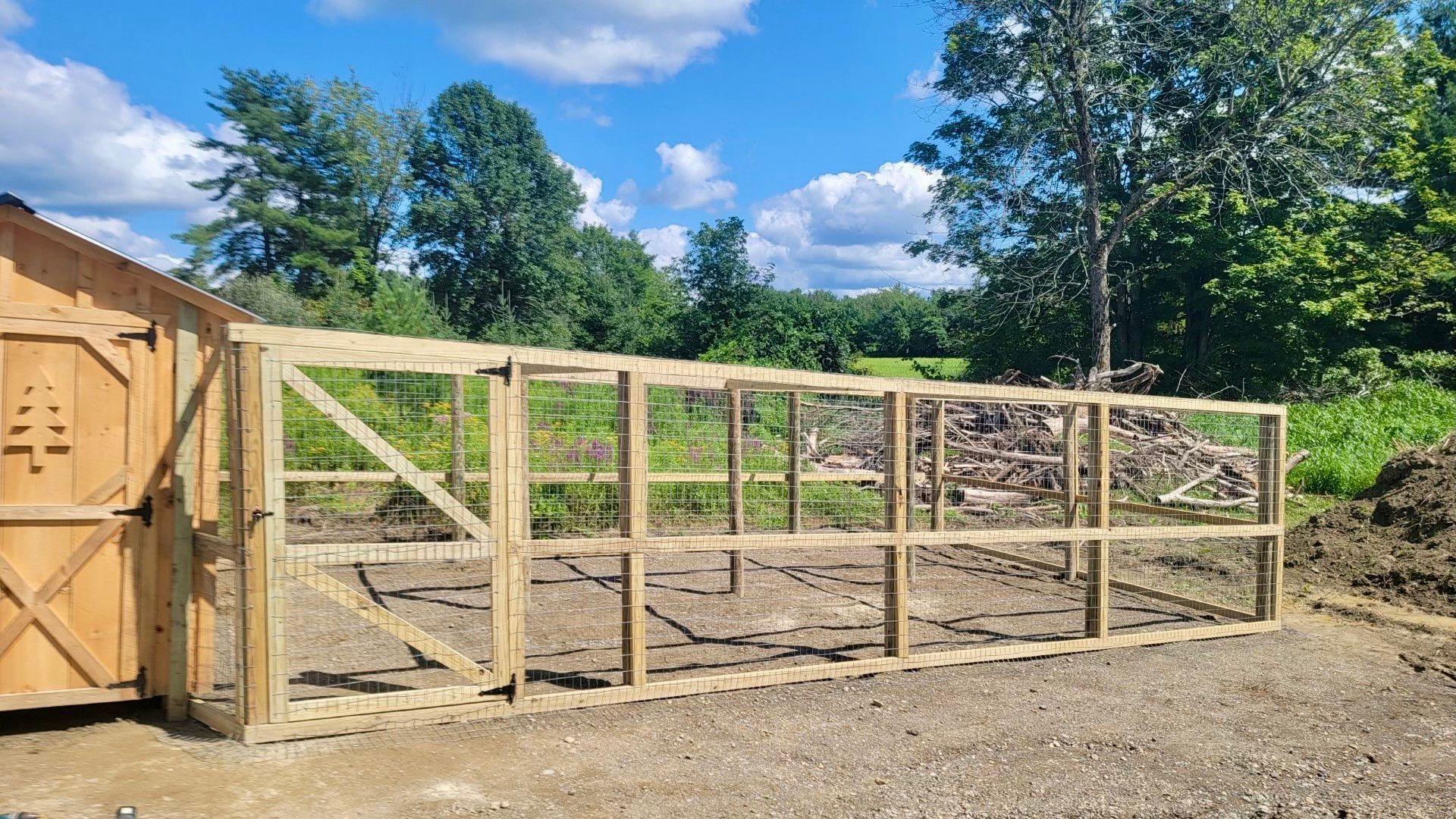 Wooden framed outdoor enclosure with wire mesh, built next to a wooden building, with a blue sky background.