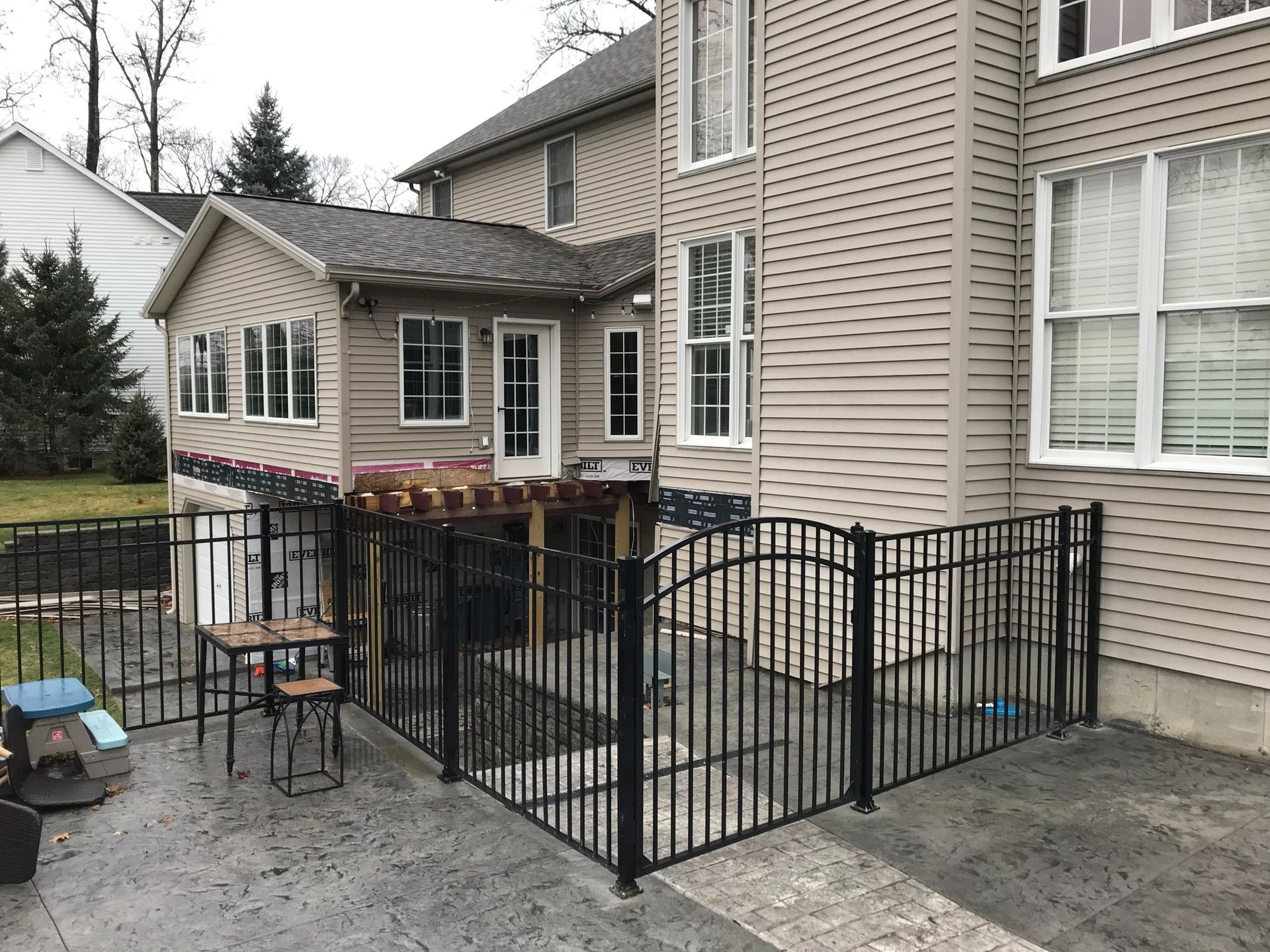 Black metal fenced patio area next to a house with a small shed-like structure attached.