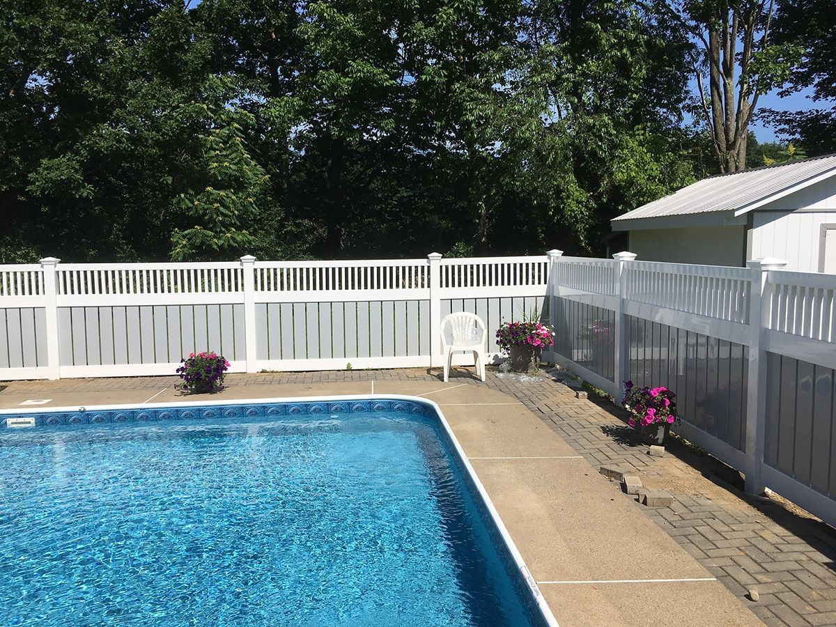 Poolside scene with a blue pool, white fence, and small shed; flowering plants in pots.