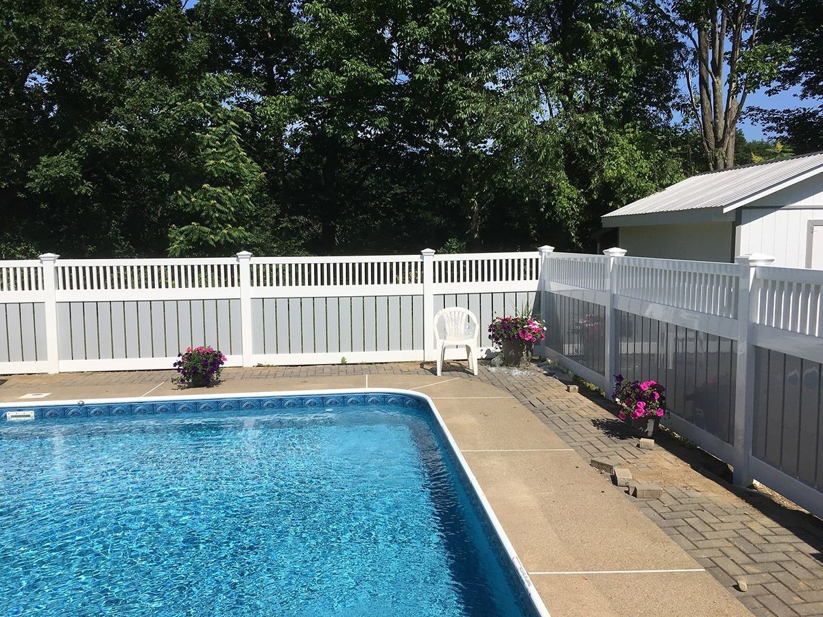 Swimming pool bordered by white fence, small shed in the background, surrounded by trees.