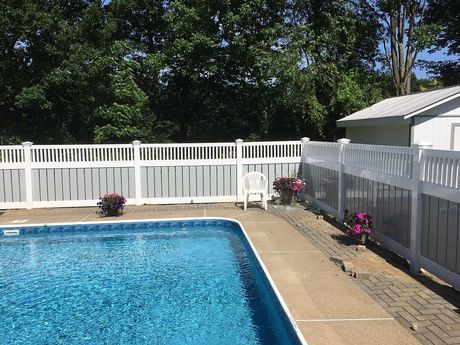 Swimming pool with white fence, landscaping, and a small shed in the background.