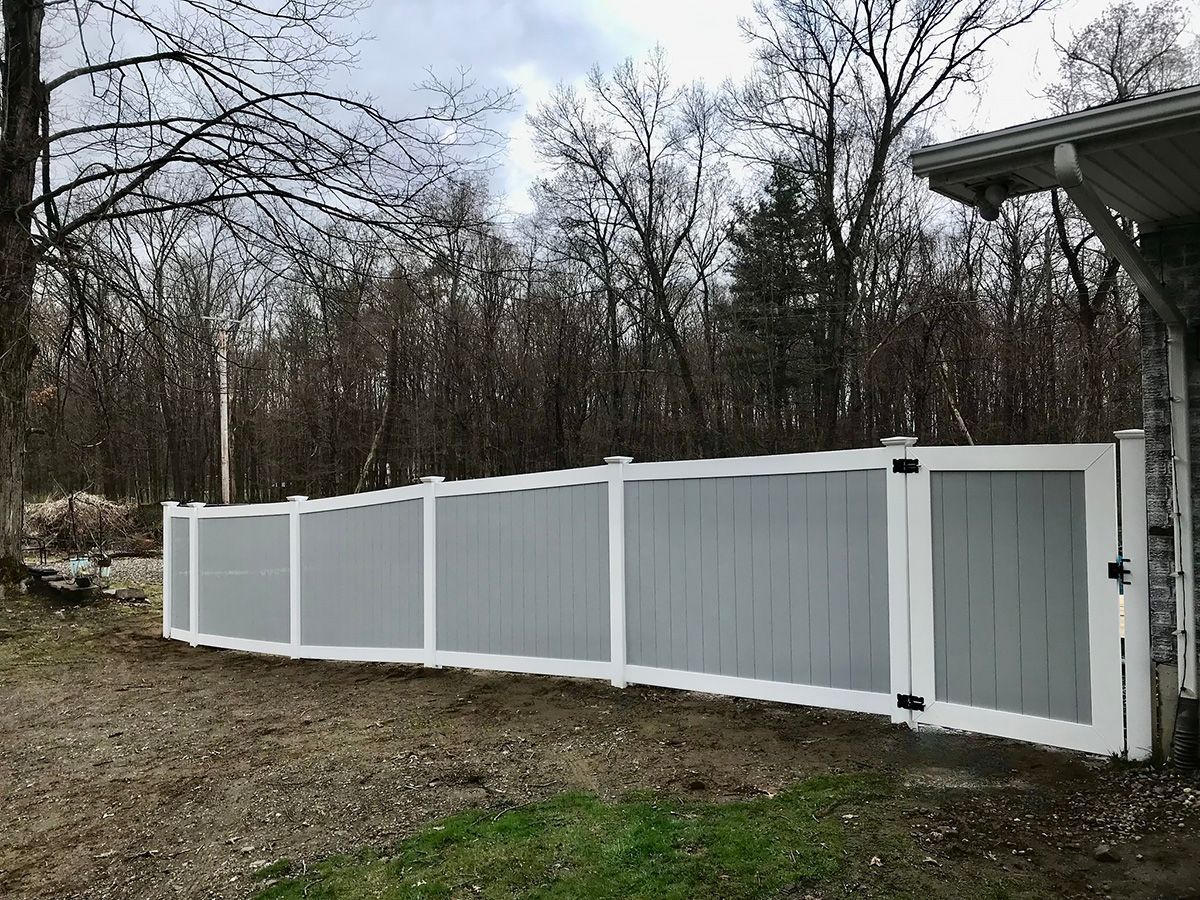 Gray and white privacy fence with a gate, in a yard with trees in the background.