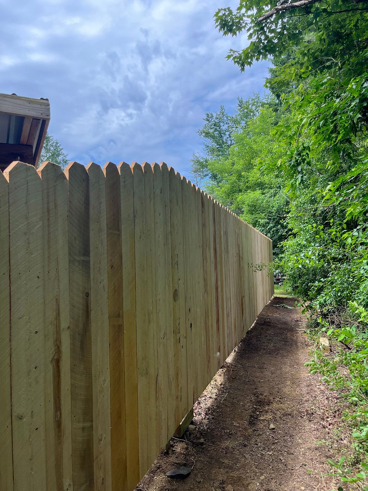 Wooden picket fence borders a path, sunlight, trees, and sky.