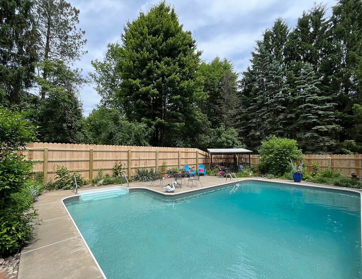 Swimming pool in backyard with wooden fence and trees.