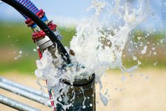 Water gushing from a pipe, splashing outwards. A black and blue hose is connected to the pipe.
