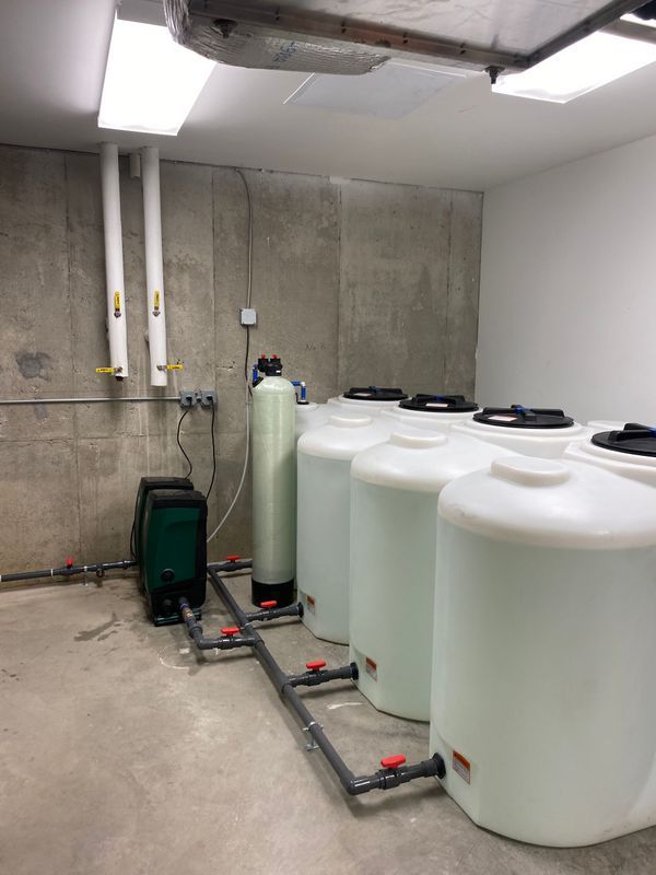 Water treatment room with several white tanks, pipes, and machinery against concrete walls and floor.