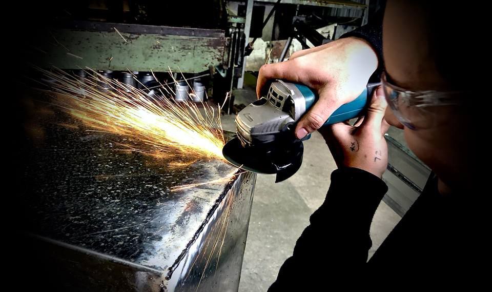 A Person Wearing Safety Glasses is Grinding a Piece of Metal — Clarry Anderson Sheet Metal Pty Ltd in Port Macquarie, NSW