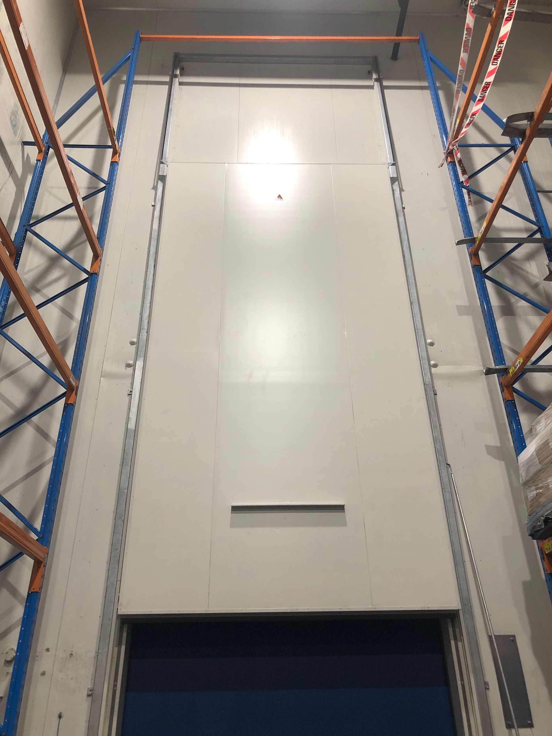 A warehouse with a large white wall and blue shelves