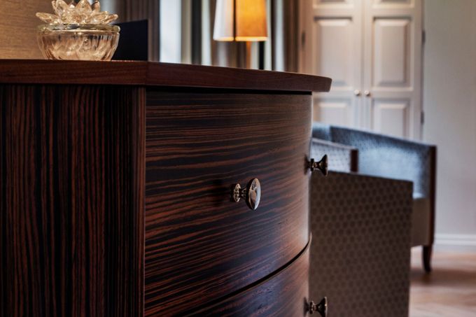 A close-up of a curved, dark wood dresser with polished silver knobs in a softly lit, modern room.