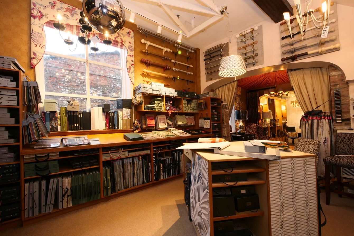 A fabric and interior design shop with shelves of samples, curtain rods on the walls, and a large central work table.