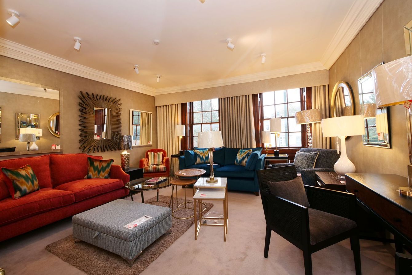 A living room with a red sofa, a grey ottoman, a blue velvet couch, and a dark wooden table with a chair.