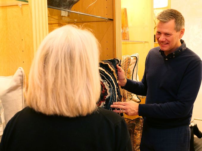 A person in a blue sweater smiling while gesturing toward patterned decorative pillows inside a shop.