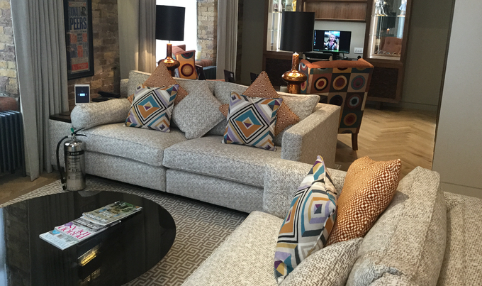 A cozy living room with a patterned sofa, matching armchair, circular black coffee table, and warm lighting.