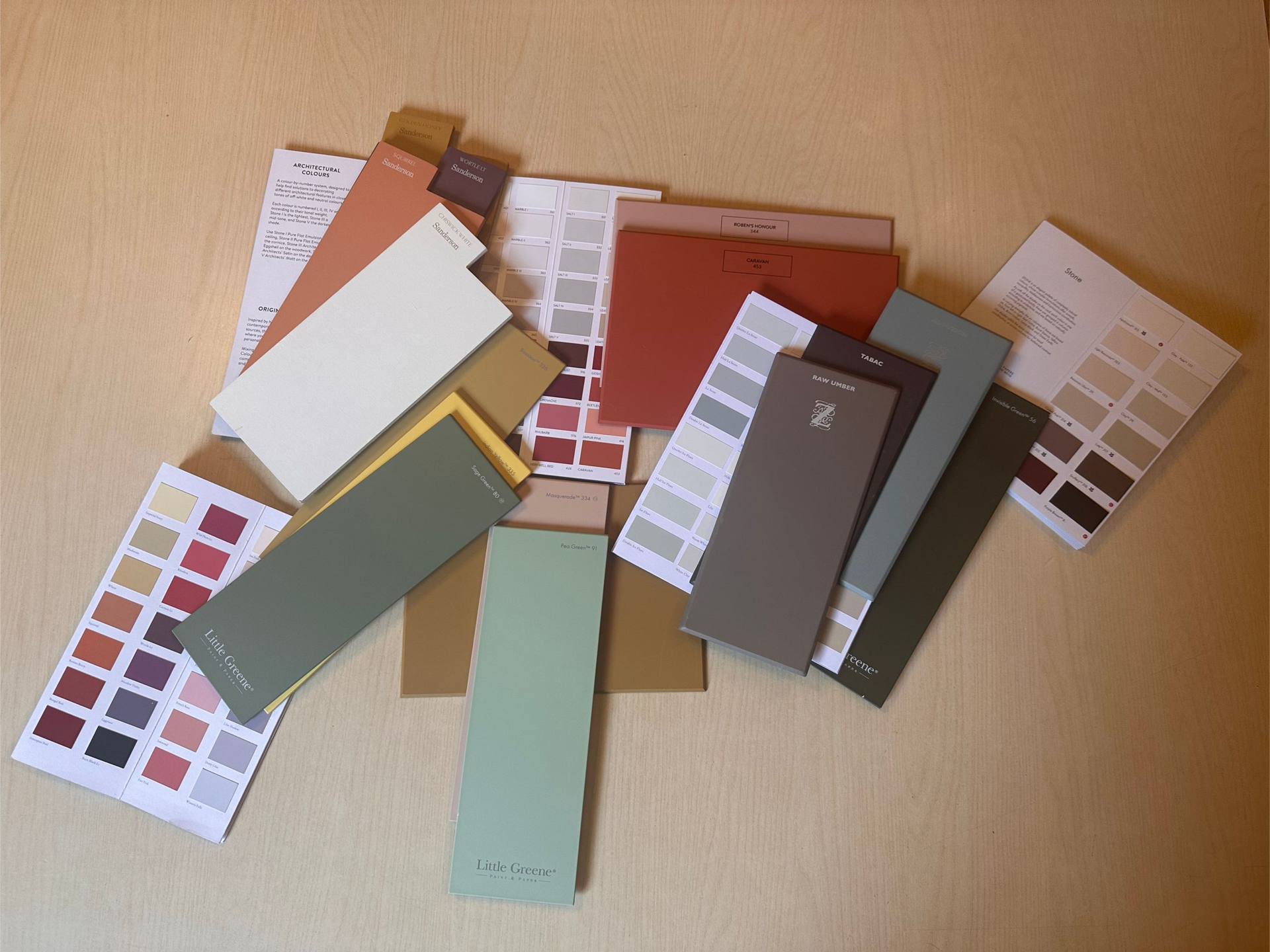 A collection of scattered paint color swatches and samples in shades of red, green, gray, and neutral beige on a table.