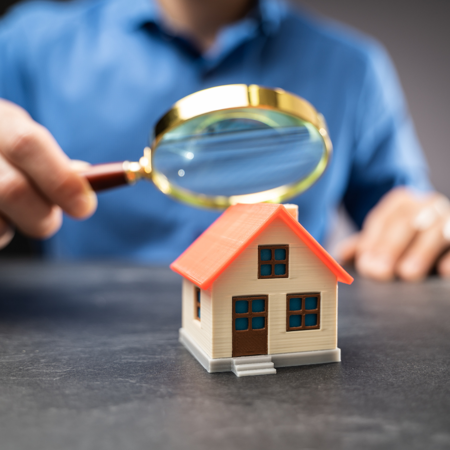 A man is looking at a model house with a magnifying glass.
