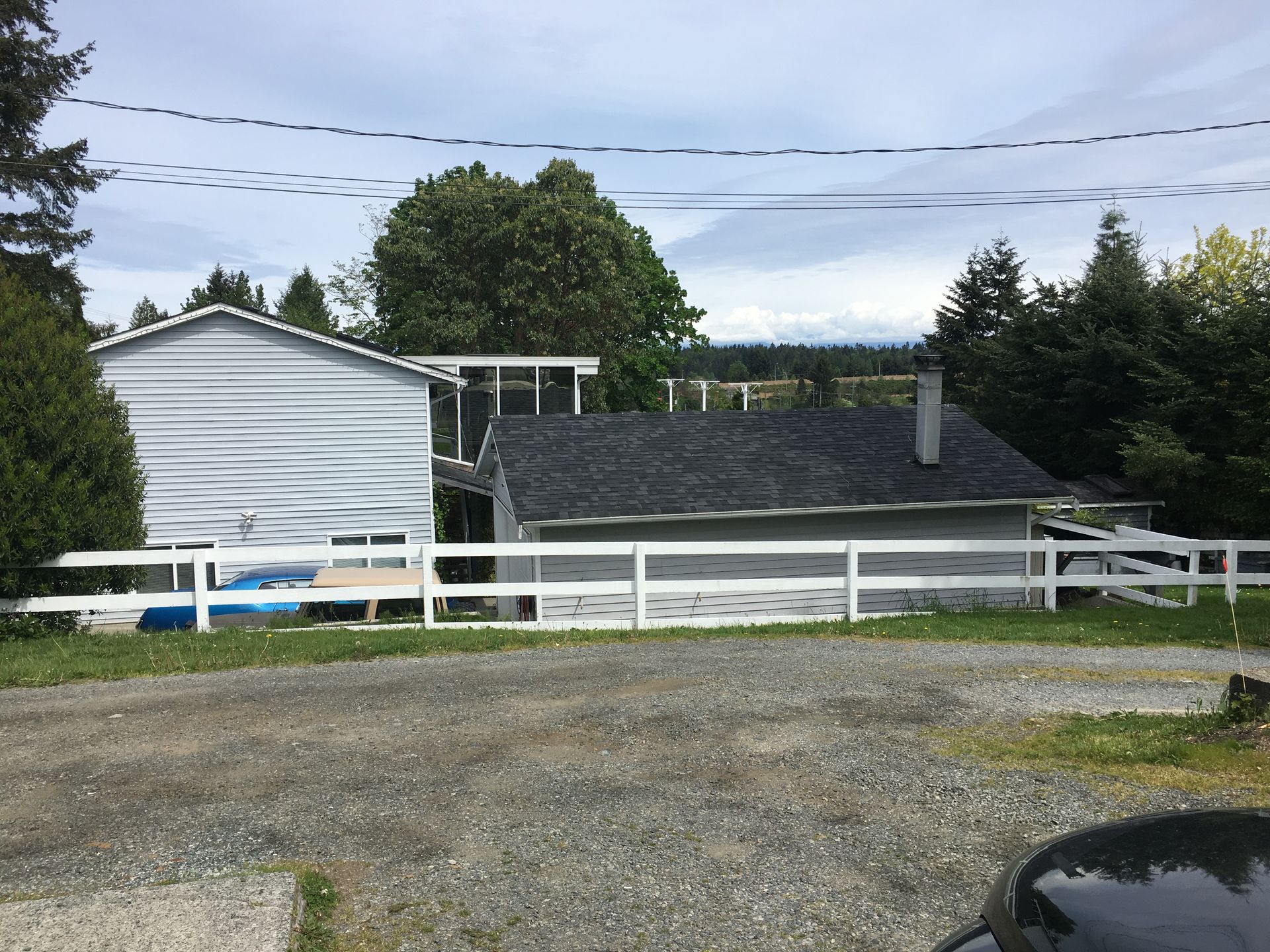 A car is parked in front of a house with a white fence.
