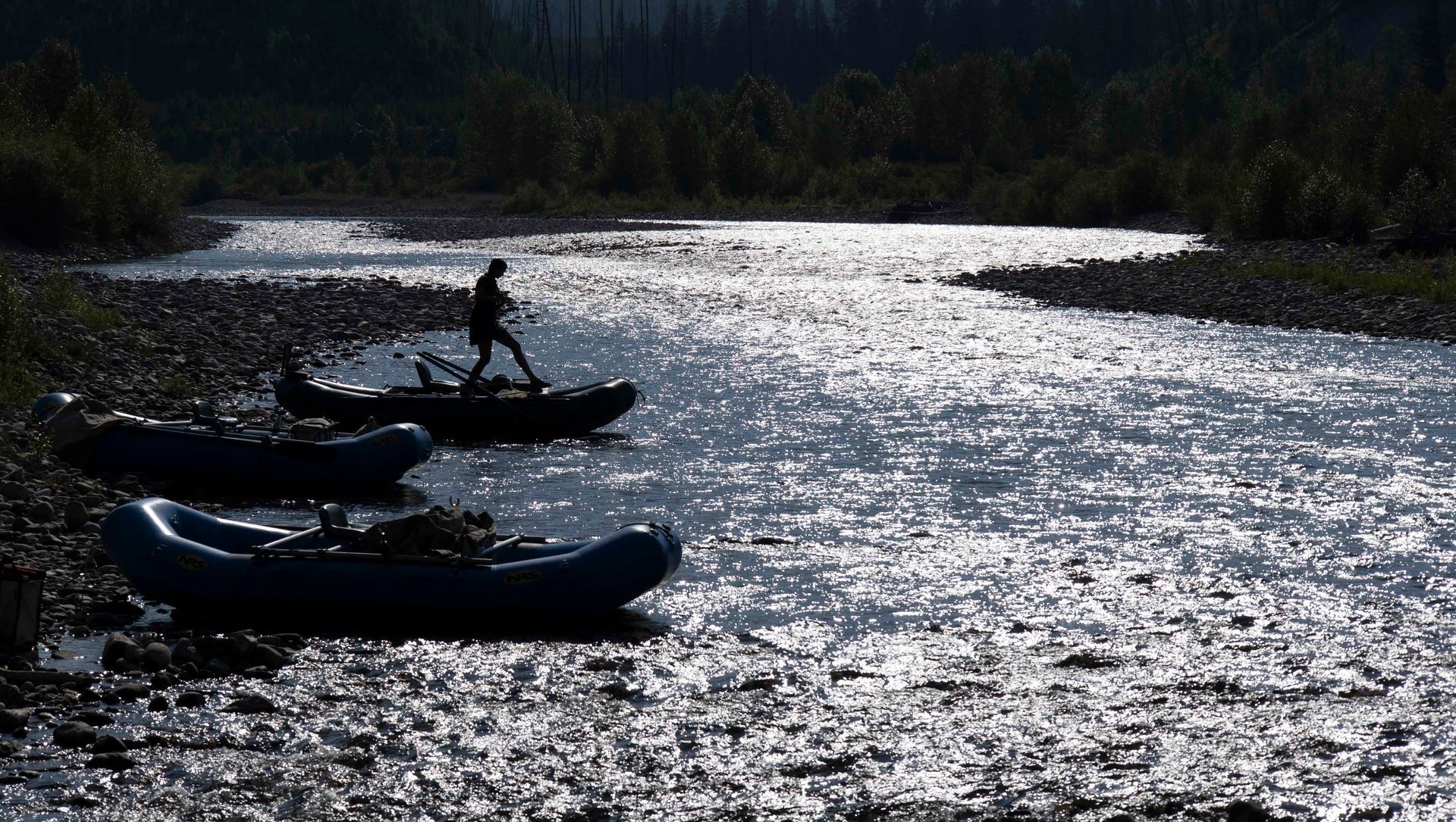 A man is standing on top of a raft in the middle of a river.