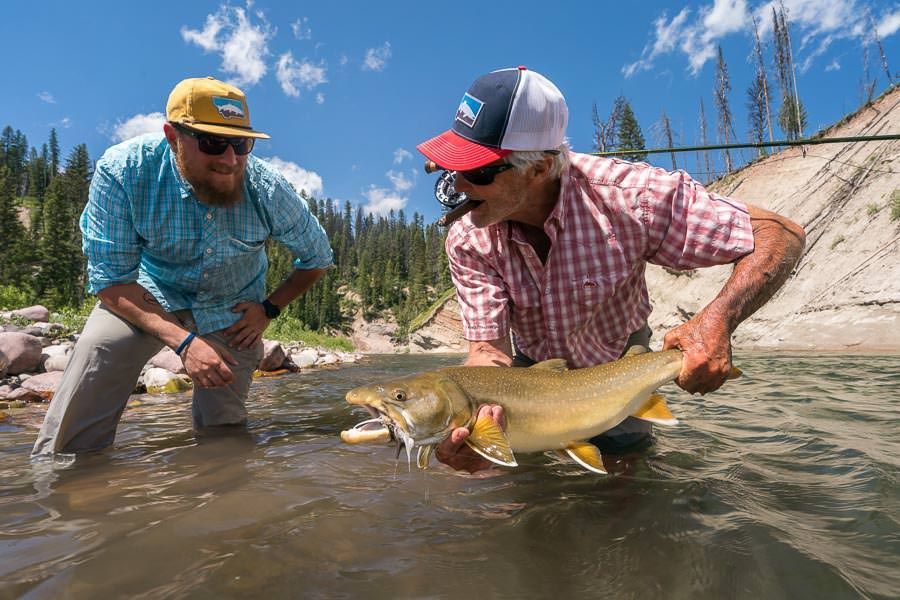 Two men are holding a large fish in a river.