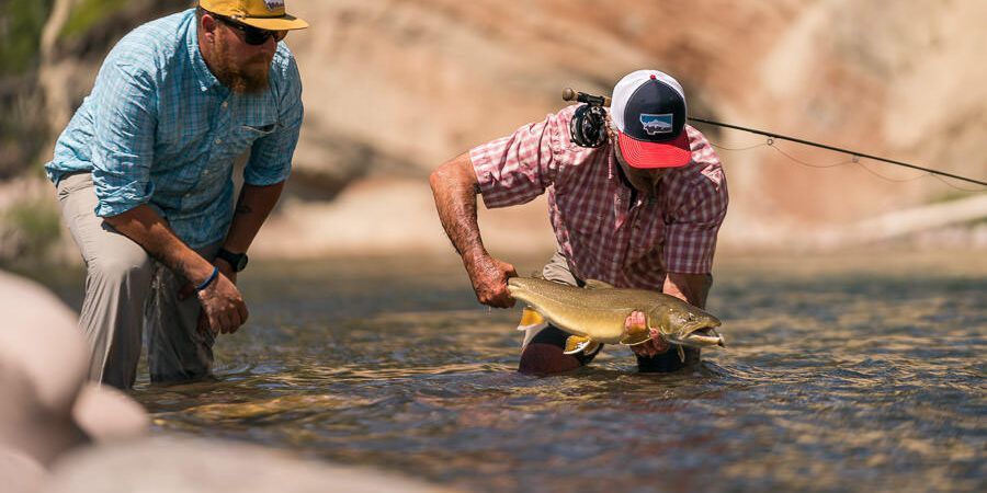 Two men are fishing in a river and one of them is holding a fish.