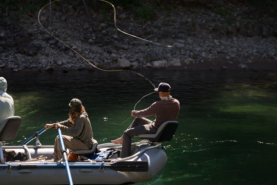 A man and a woman are fishing in a boat on a river.