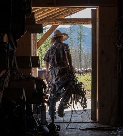 A man in a cowboy hat is standing in a barn with a horse.