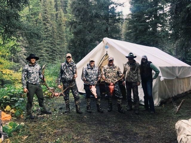 A group of people standing in front of a tent in the woods.