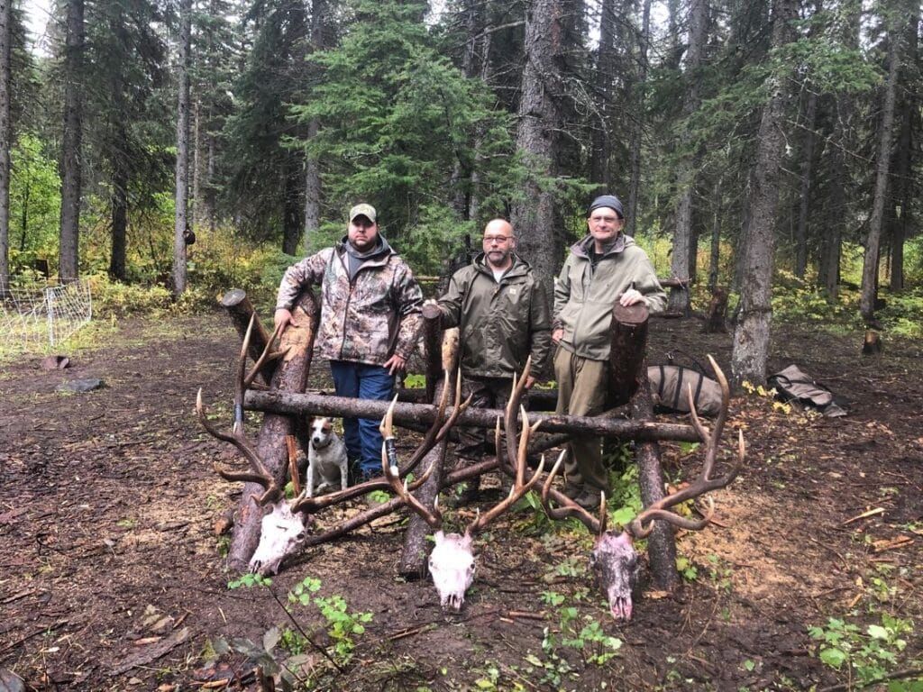 three men posing with dear skull trophies