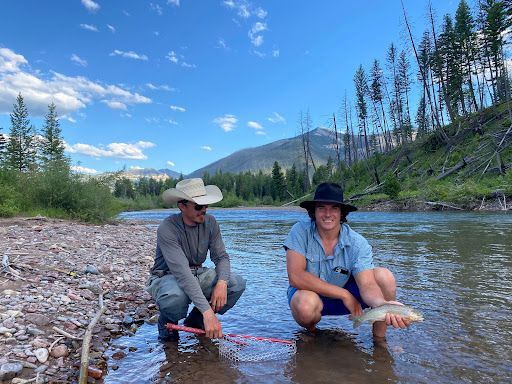 Two men are kneeling in the water holding a fish.